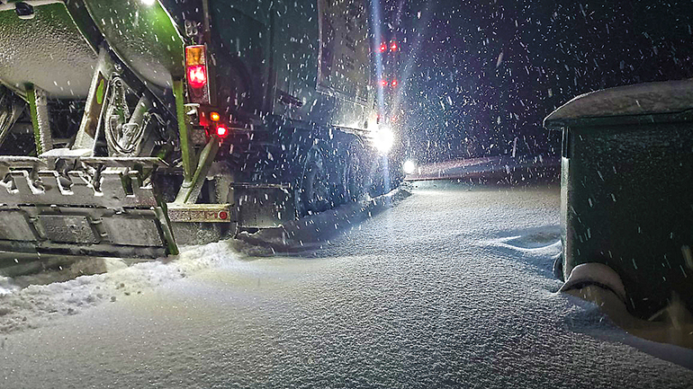 En sopbil och ett sopkärl på en väg med snö.