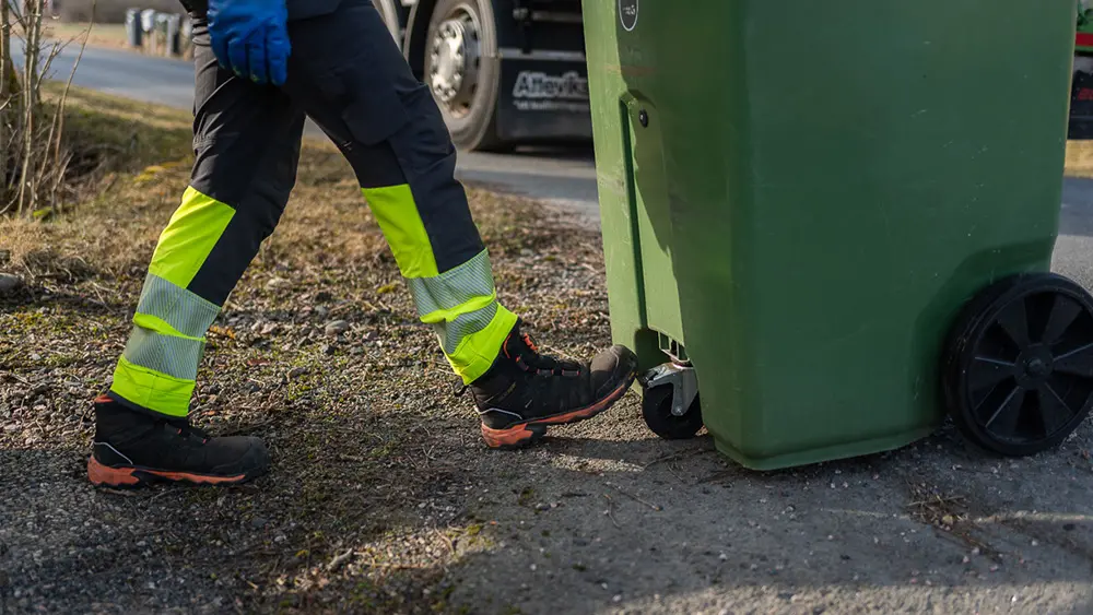 En fot trycker ner bromsen på ett sopkärl.