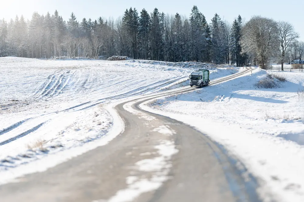 En sopbil åker på en väg i vinterlandskap